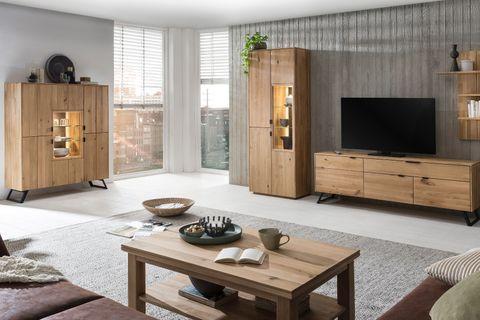 Modernes Wohnzimmer mit hellen Holzmöbeln, darunter eine Vitrine, ein Sideboard und ein Couchtisch. Ein großer Fernseher steht auf dem Sideboard, während die Einrichtung mit grünen Pflanzen und Büchern dekoriert ist.