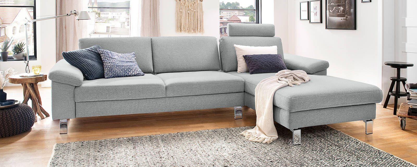 Helles Ecksofa in modernem Design mit grauem Stoffbezug und Kissen, ergänzt durch eine gemütliche Wohnzimmereinrichtung.