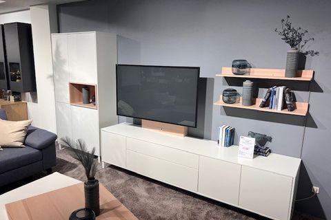 Moderne Wohnwand mit Fernseher, offenen Regalen und geschlossenen Schränken in Weiß und Holzoptik, arrangiert vor einer grauen Wand.