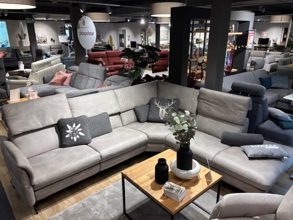 Moderne Couchgarnitur Calimero in hellem Grau mit verstellbaren Rückenlehnen und Dekokissen, präsentiert in einem wohnlichen Showroom.