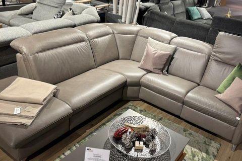 Große Ledercouchgarnitur Louisiana in modernem Grau mit Eckdesign, dekoriert mit grünen und beigen Kissen. Beistelltisch mit Metallplatte und dekorativen Elementen davor