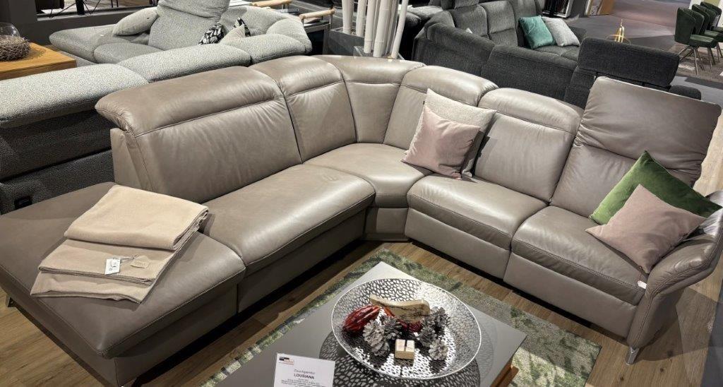 Große Ledercouchgarnitur Louisiana in modernem Grau mit Eckdesign, dekoriert mit grünen und beigen Kissen. Beistelltisch mit Metallplatte und dekorativen Elementen davor