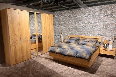 Schlafzimmer mit Kleiderschrank in Holzoptik mit Spiegeltüren, Doppelbett und Nachttischen vor einer Steinwand.