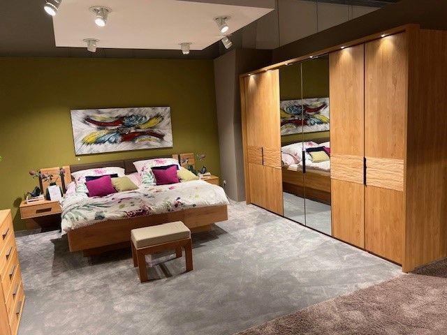 Modernes Schlafzimmer mit Kleiderschrank mit Spiegelfronten, Bett aus Holz, Nachttischen und farbenfroher Dekoration vor einer grünen Wand.