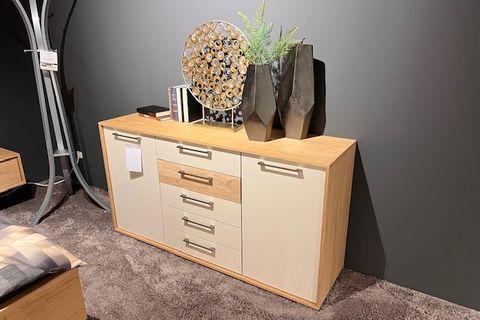 Moderne Kommode mit Holz- und Weißelementen, dekoriert mit Vasen und Accessoires, auf einem Teppichboden.