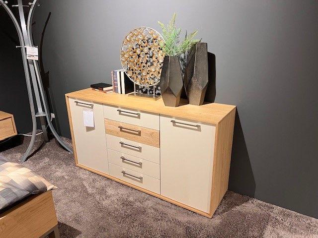 Moderne Kommode mit Holz- und Weißelementen, dekoriert mit Vasen und Accessoires, auf einem Teppichboden.