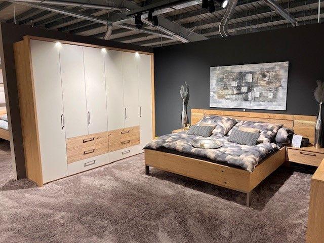 Modernes Schlafzimmer mit Holz- und Weißelementen, bestehend aus Kleiderschrank, Doppelbett und Nachttischen, auf einem weichen Teppichboden.