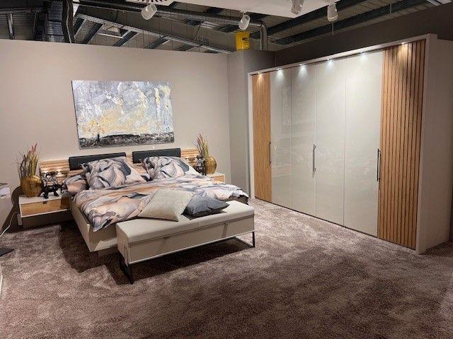 Schlafzimmer mit modernem Kleiderschrank mit Holz- und Glanzfronten, Bett mit gepolstertem Kopfteil und Bettbank, dekoriert mit abstrakter Kunst.