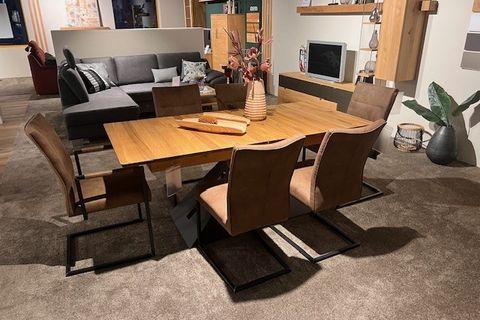 Essgruppe mit Holztisch und sechs braunen Stühlen auf einem Teppich, modern eingerichtet in einem gemütlichen Wohnzimmer.