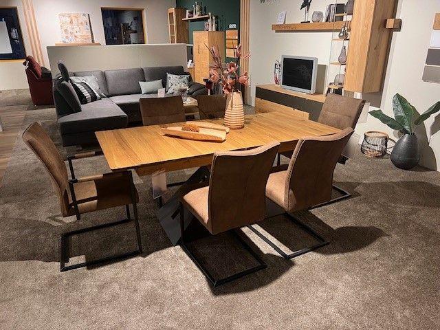 Essgruppe mit Holztisch und sechs braunen Stühlen auf einem Teppich, modern eingerichtet in einem gemütlichen Wohnzimmer.