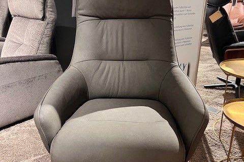 Grauer Relaxsessel mit ergonomischer Rückenlehne und Drehfuß, präsentiert auf einem Teppichboden in einer modernen Ausstellung.