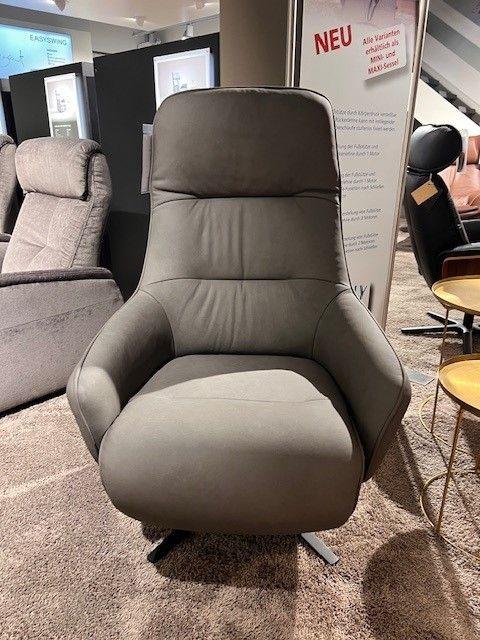 Grauer Relaxsessel mit ergonomischer Rückenlehne und Drehfuß, präsentiert auf einem Teppichboden in einer modernen Ausstellung.