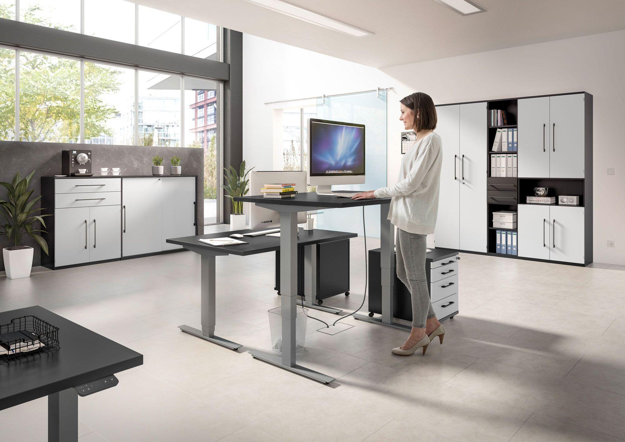Flexibler Arbeitsplatz mit höhenverstellbarem Schreibtisch und ergonomischem Design in einem modernen Büro mit viel Stauraum und großen Fenstern.