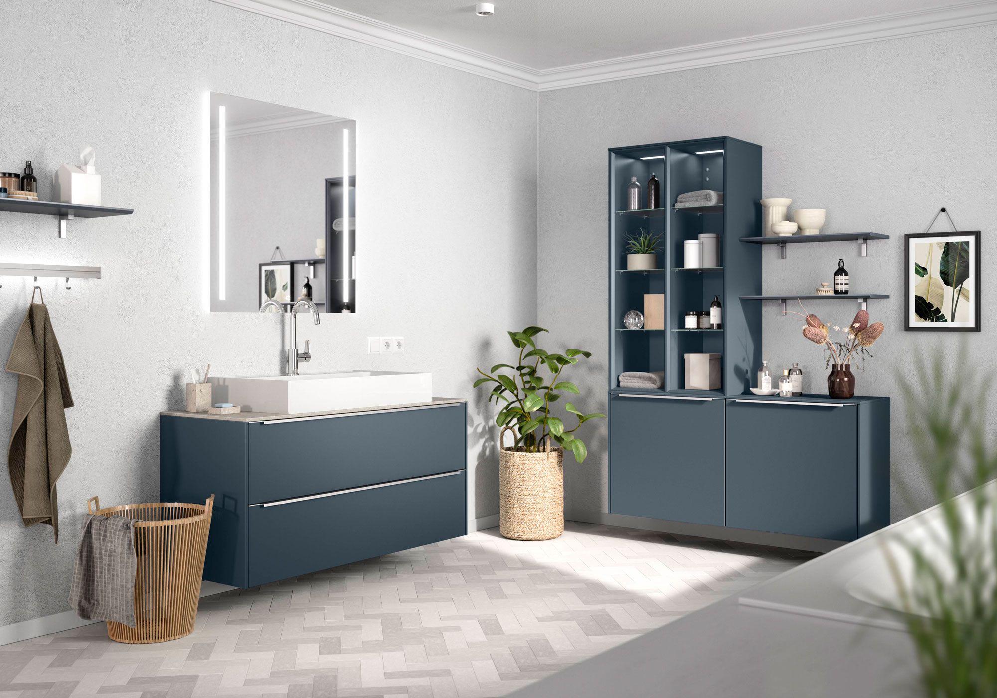 Elegantes Badezimmer mit blauen Schränken und einem beleuchteten Spiegel, kombiniert mit modernen Regalen und dekorativen Pflanzen.