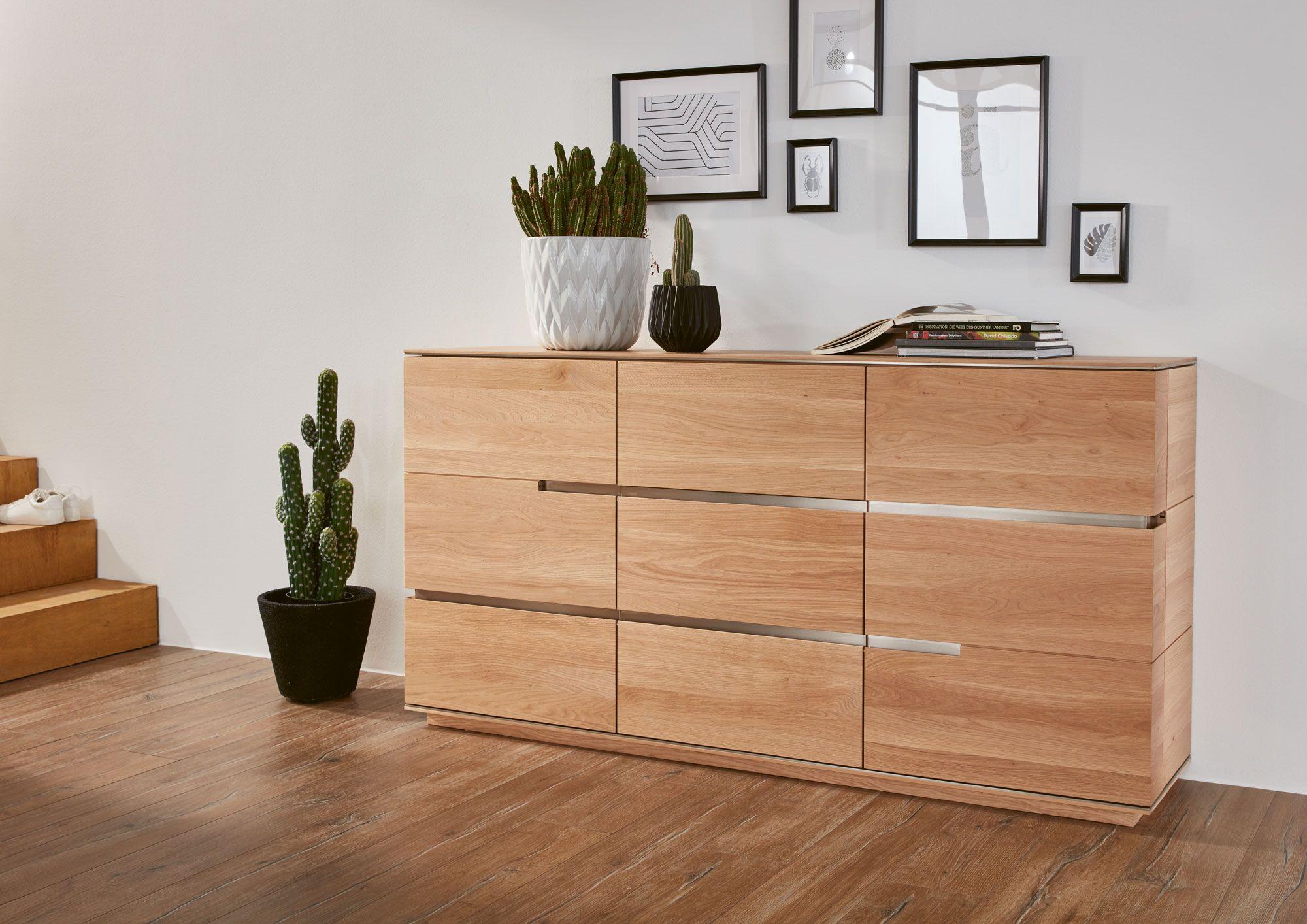 Moderne Holzkommode mit klaren Linien, dekoriert mit Pflanzen und eingerahmten Bildern, auf einem warmen Holzfußboden.
