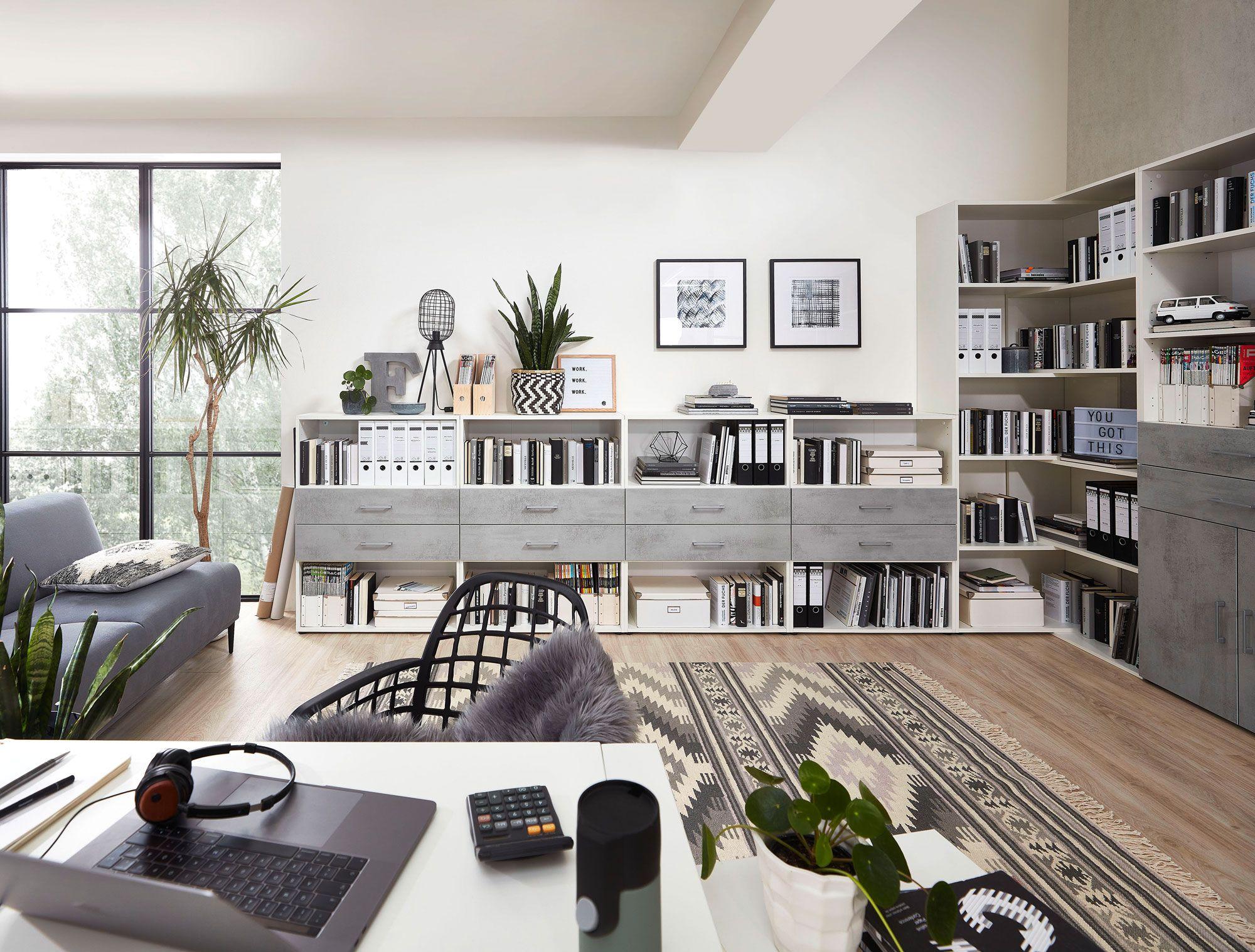 Modernes Homeoffice mit großzügigen Regalen, Schubladen und einem Schreibtisch. Stilvolle Betonoptik und Tageslicht sorgen für ein angenehmes Arbeitsambiente.