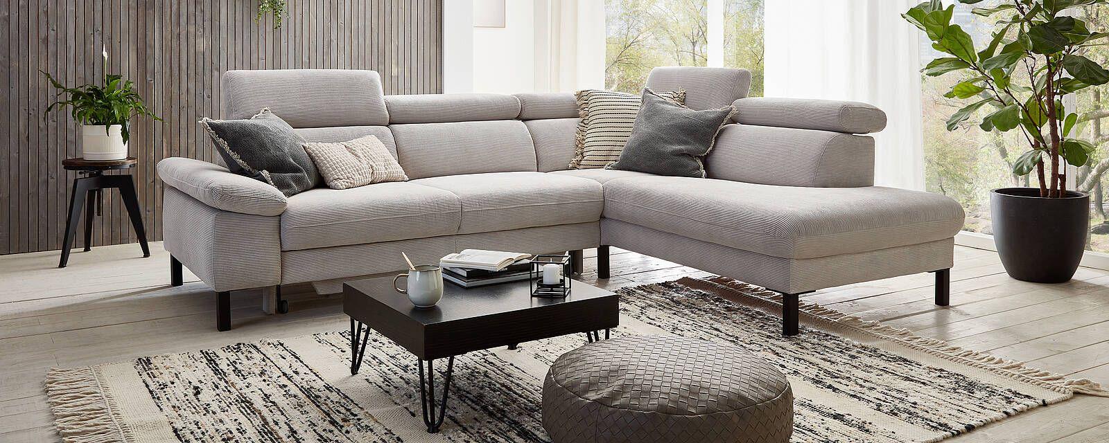 Beiges Ecksofa in einem harmonischen Wohnzimmer, dekoriert mit Pflanzen und einem gemusterten Teppich.