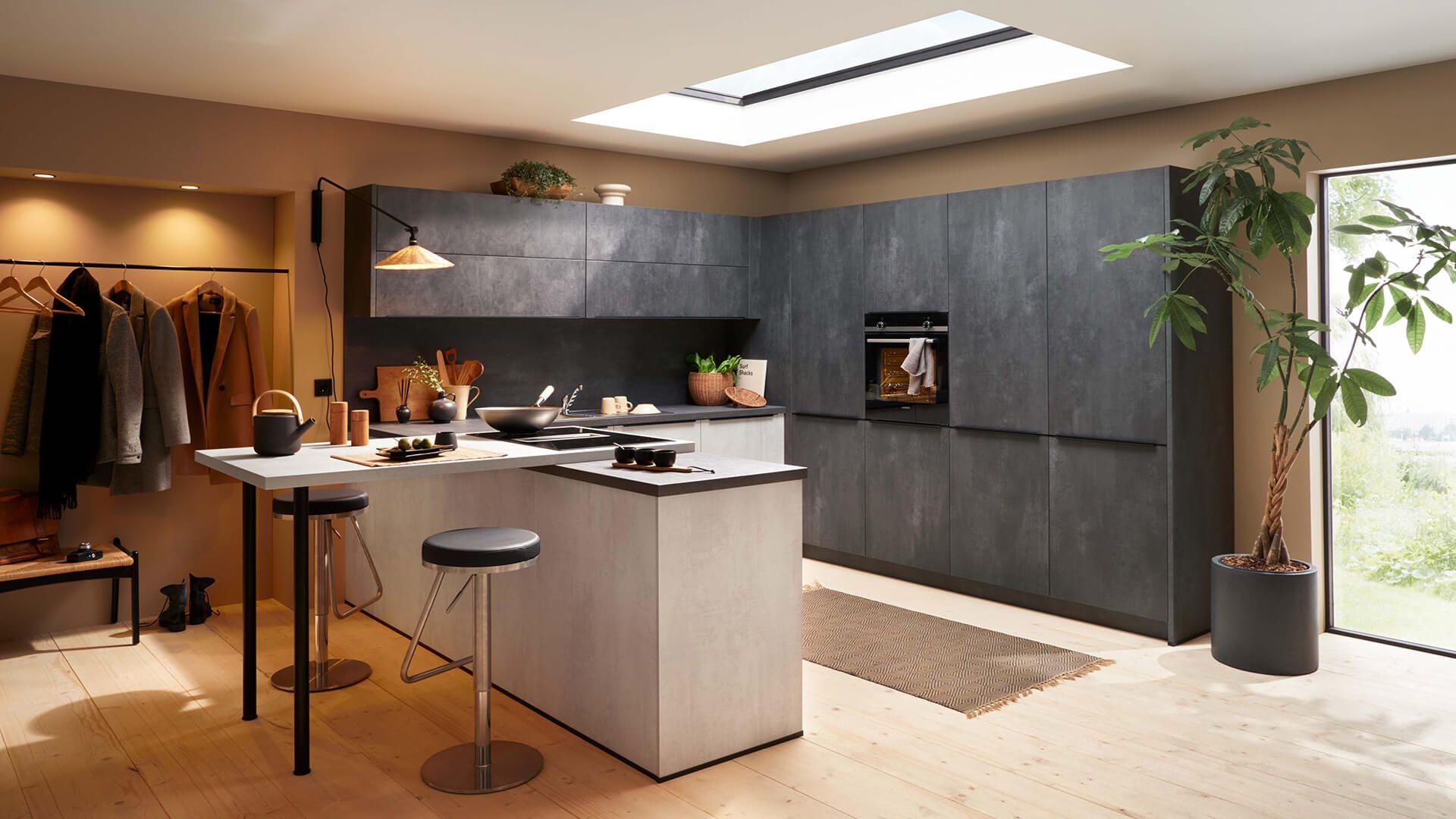 Moderne Küche mit dunklen Fronten in Betonoptik, heller Holzarbeitsplatte, kleiner Frühstücksinsel mit Barhockern, großem Dachfenster und integriertem Garderobenbereich mit hängenden Mänteln. Moderne Küche mit dunklen Fronten in Betonoptik, heller Holzarbeitsplatte, kleiner Frühstücksinsel mit Barhockern, großem Dachfenster und integriertem Garderobenbereich mit hängenden Mänteln.