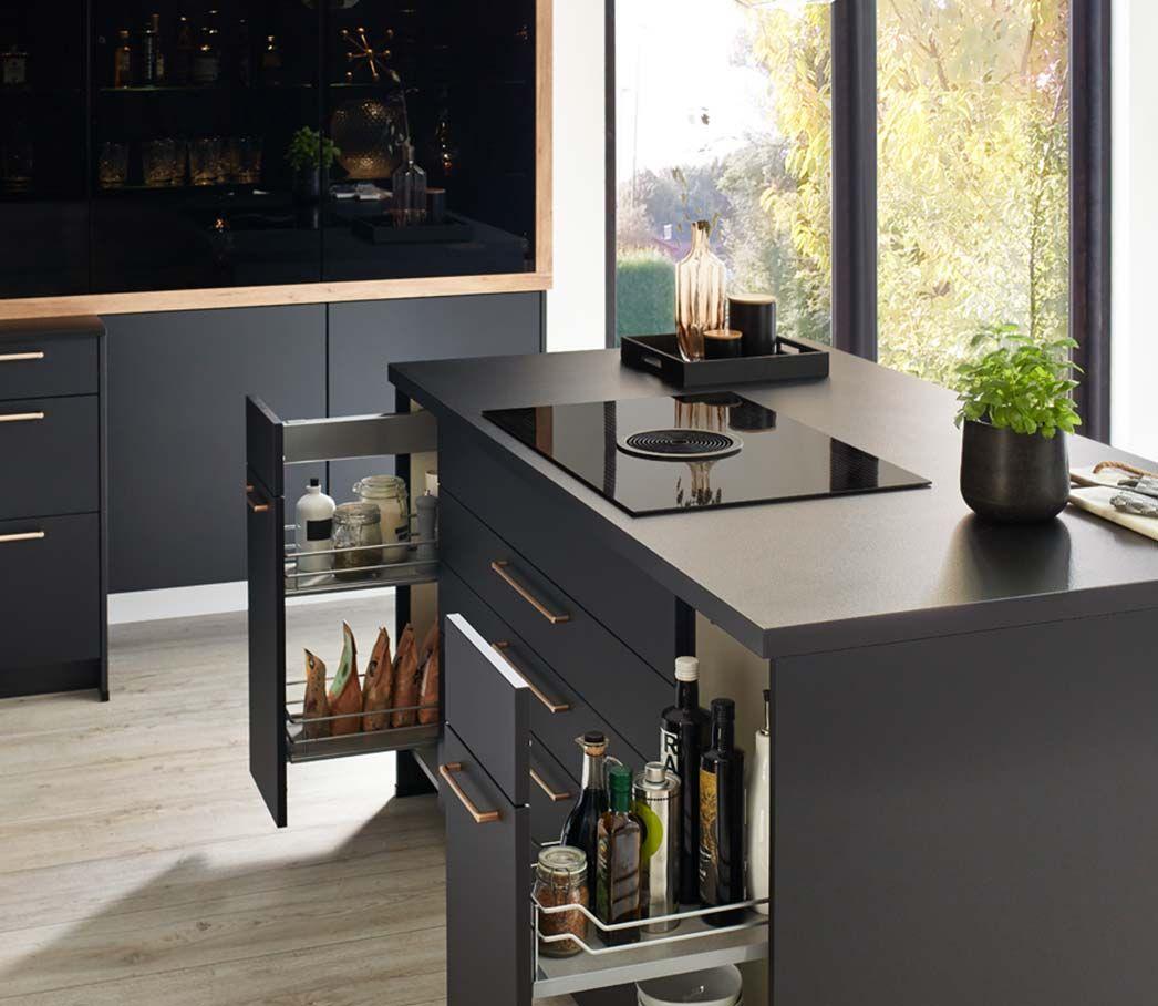 Schwarze Kücheninsel mit ausziehbaren Schubladen für Gewürze und Flaschen, beleuchtet von natürlichem Tageslicht.