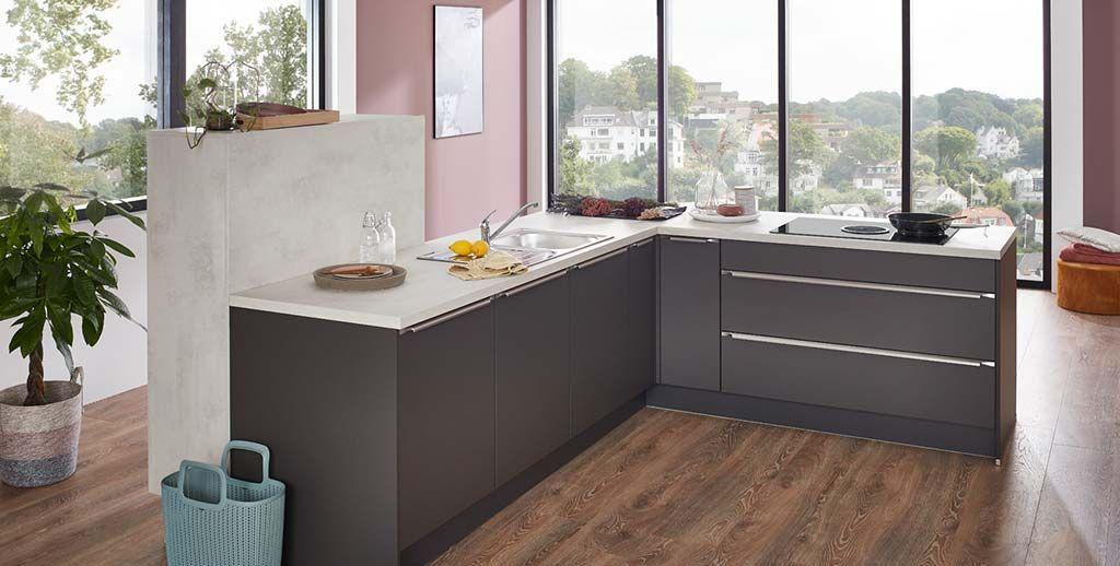 Detailansicht einer modernen L-förmigen Küche mit dunklen Fronten und heller Arbeitsplatte, kombiniert mit einem Panoramaausblick durch große Fenster.