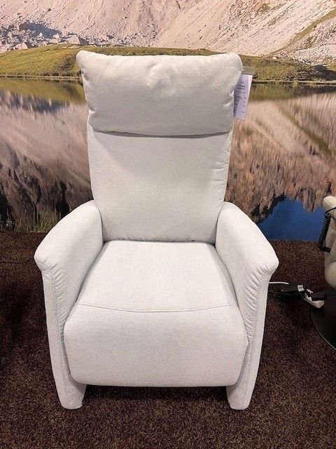 Heller Relaxsessel mit gepolsterter Rückenlehne, verstellbarem Kopfteil und weichen Armlehnen, auf einem braunen Teppichboden vor einer Landschaftskulisse.