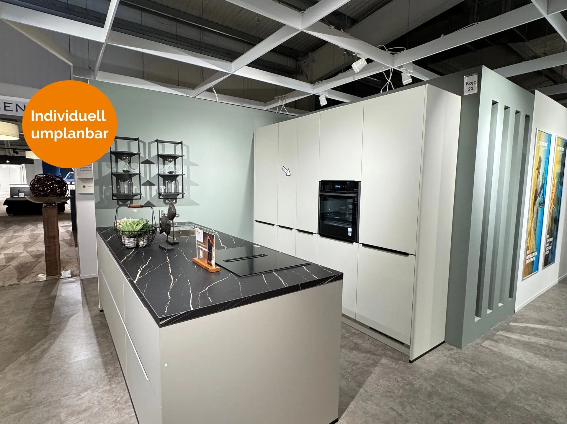 Minimalistische Küche in hellem Graugrün mit grifflosen Fronten, schwarzer Marmor-Arbeitsplatte mit weißer Maserung, großer Kochinsel mit Induktionskochfeld, Hochschrankzeile mit integrierten Geräten und offenem Metallregal.